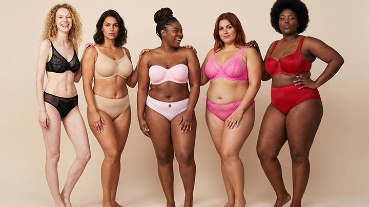 A diverse group of five smiling women standing in a row, confidently wearing comfortable, non-padded HSIA bras that provide a natural silhouette without showing nipples through their shirts.