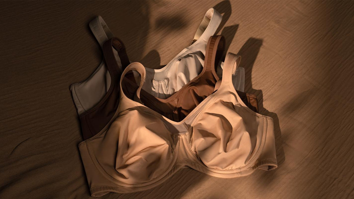 Three supportive bras in nude, brown and white flat lay on warm wood surface, showing everyday comfortable options for large busts