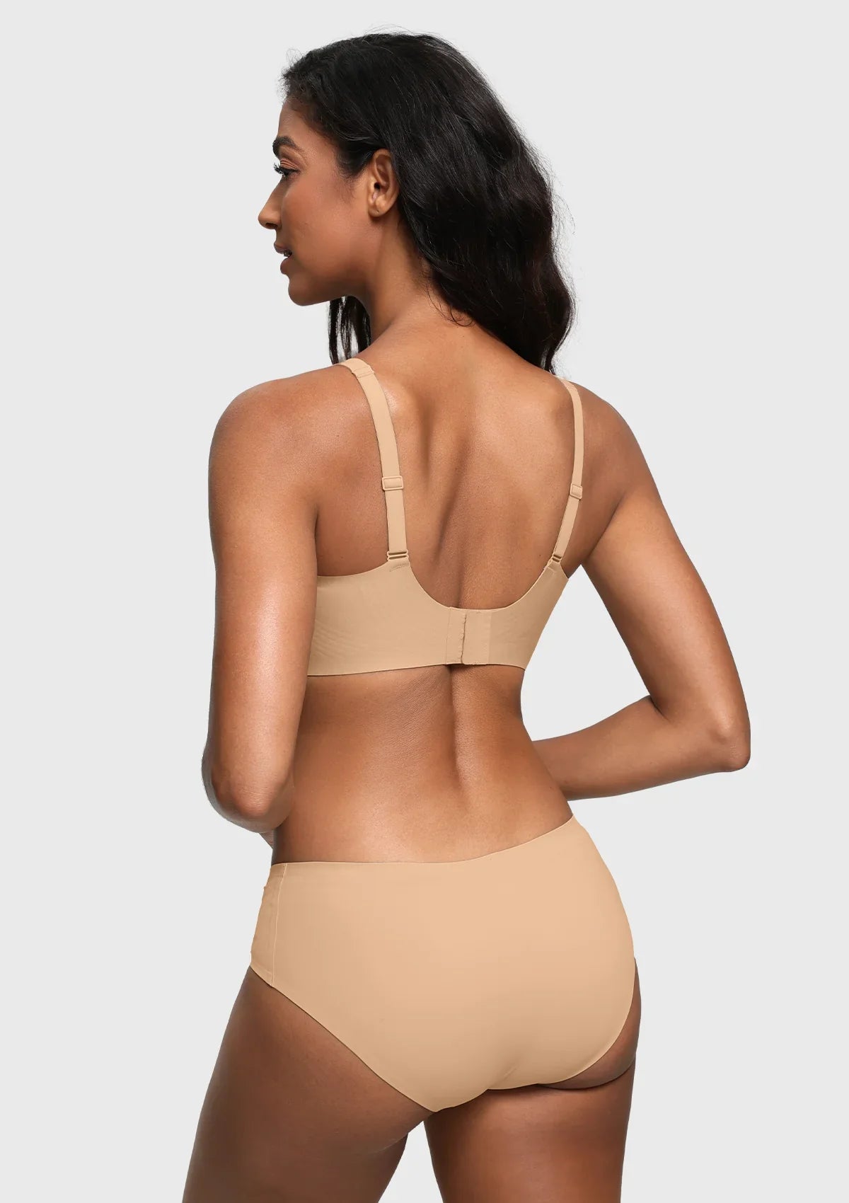 A woman shown from the back wearing a light beige seamless bra and matching high-waisted briefs against a light gray studio background.