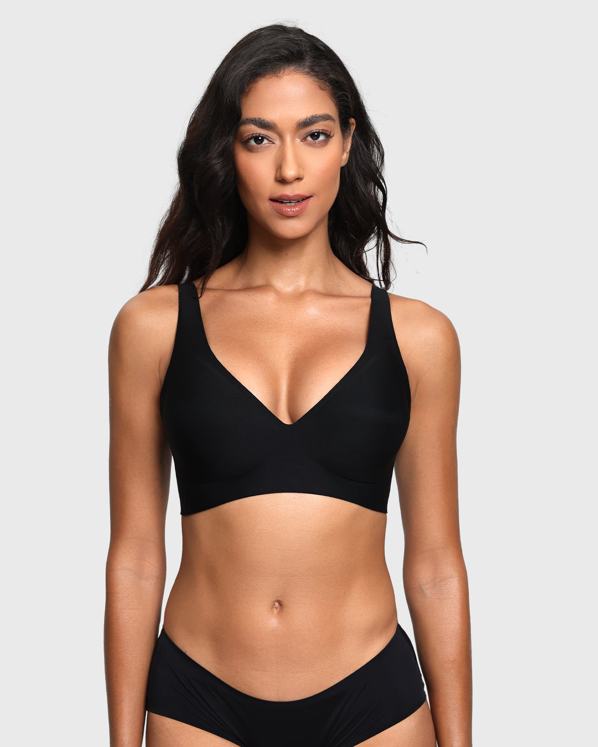 A woman modeling a black two-piece bikini set against a light gray studio background. The set includes a V-neck bikini top with wide shoulder straps and matching high-cut bikini bottoms.