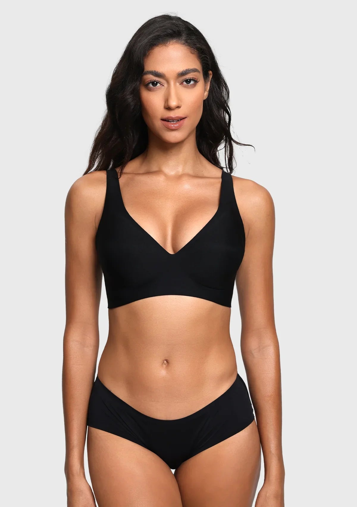 A woman modeling a black two-piece bikini set against a light gray studio background. The set includes a V-neck bikini top with wide shoulder straps and matching high-cut bikini bottoms.