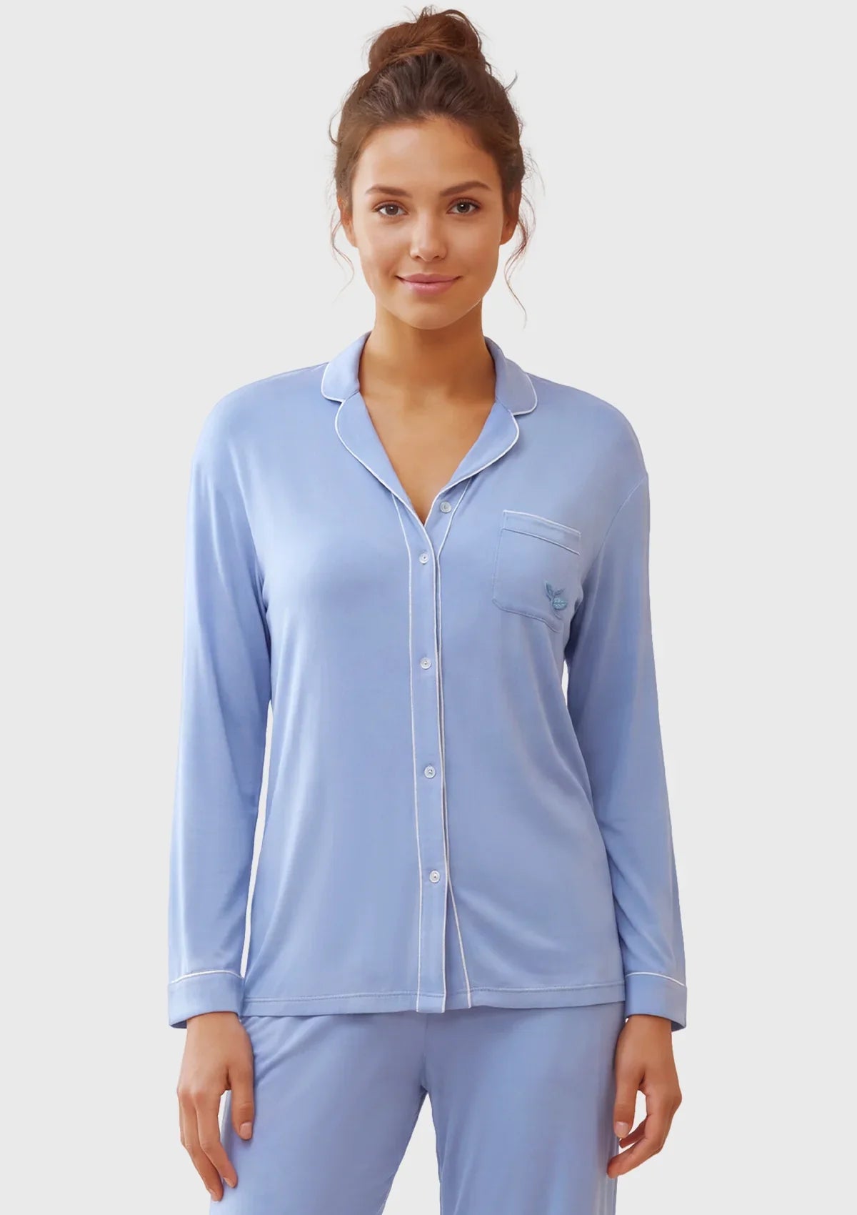 A woman modeling a light blue long-sleeve pajama set with a button-front top and matching pants against a plain light gray studio background.