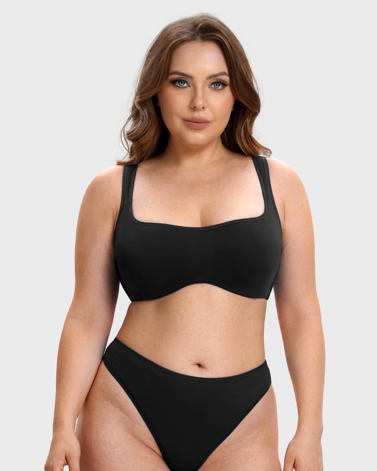 A woman modeling a black two-piece bikini set against a light gray studio background. The set includes a scoop-neck bikini top with wide straps and matching high-cut bikini bottoms.
