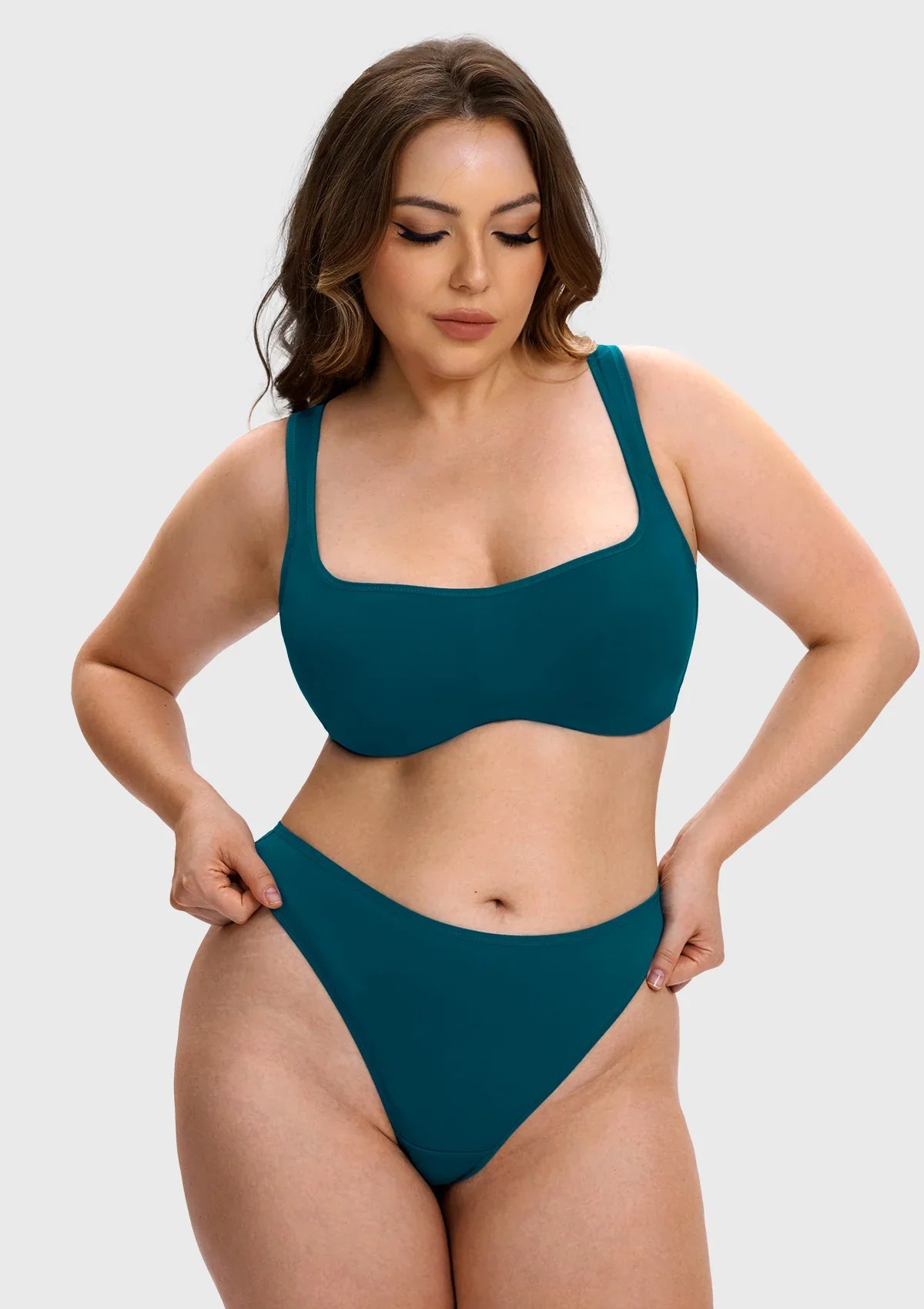 A woman modeling a solid teal two-piece bikini set against a light gray studio background.