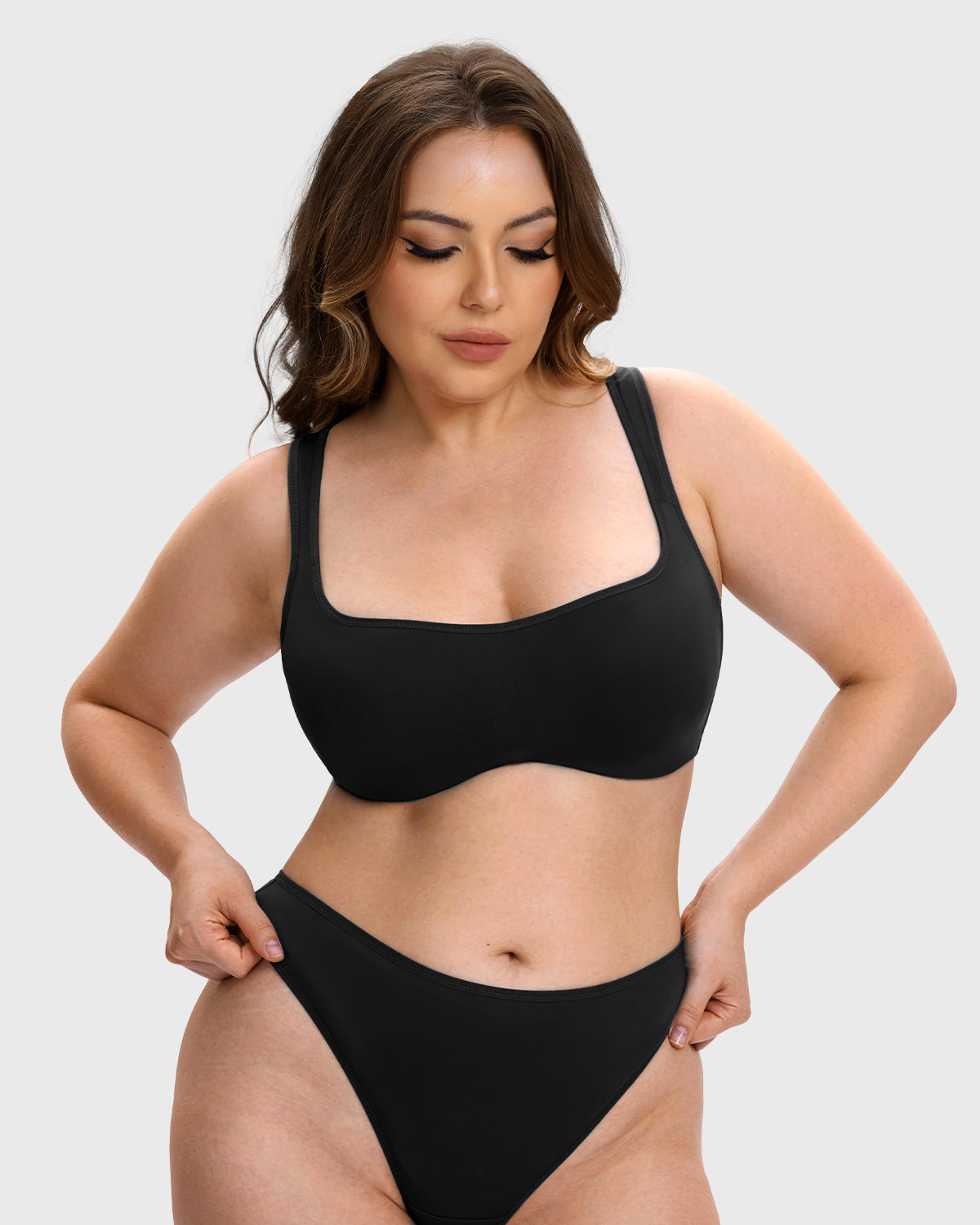 A woman modeling a solid black two-piece bikini set against a light gray studio background.