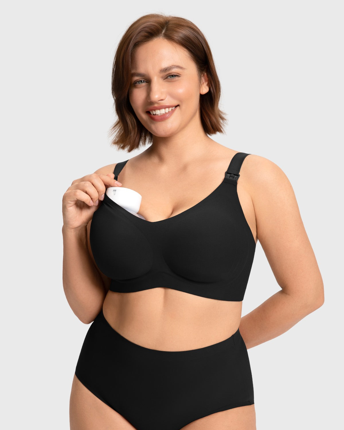 Model demonstrating hands-free pumping by securing a breast pump inside the black wireless nursing bra cup, providing convenience for multitasking moms.