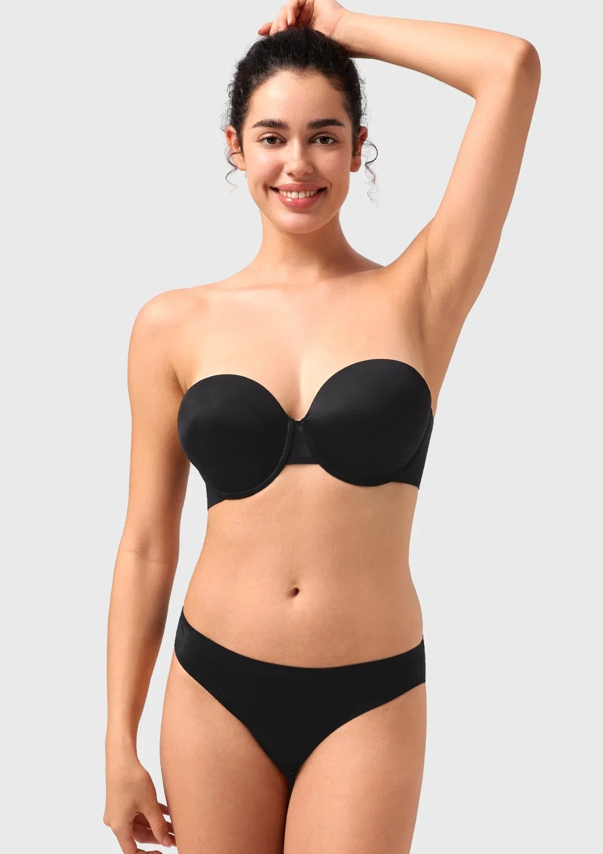 Smiling woman raising her arms in the black stay-put strapless bra, demonstrating unwavering support without any shifting or slipping.