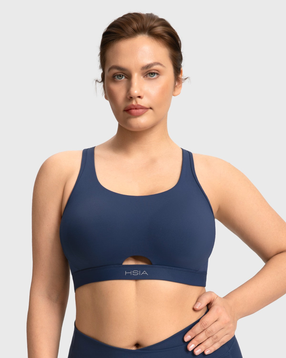 Front view of woman wearing the navy blue Aura criss-cross sports bra with breathable keyhole