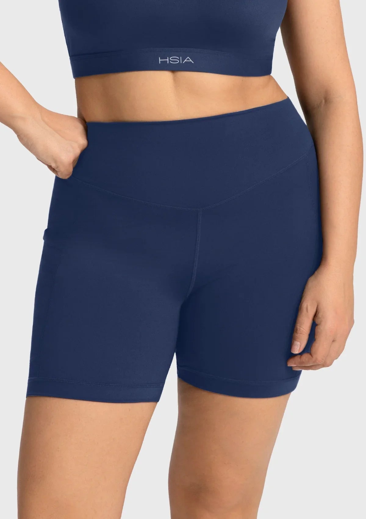 Confident woman posing with her hands in the side pockets of the navy blue athletic shorts with pockets, blending high fashion with gym functionality.