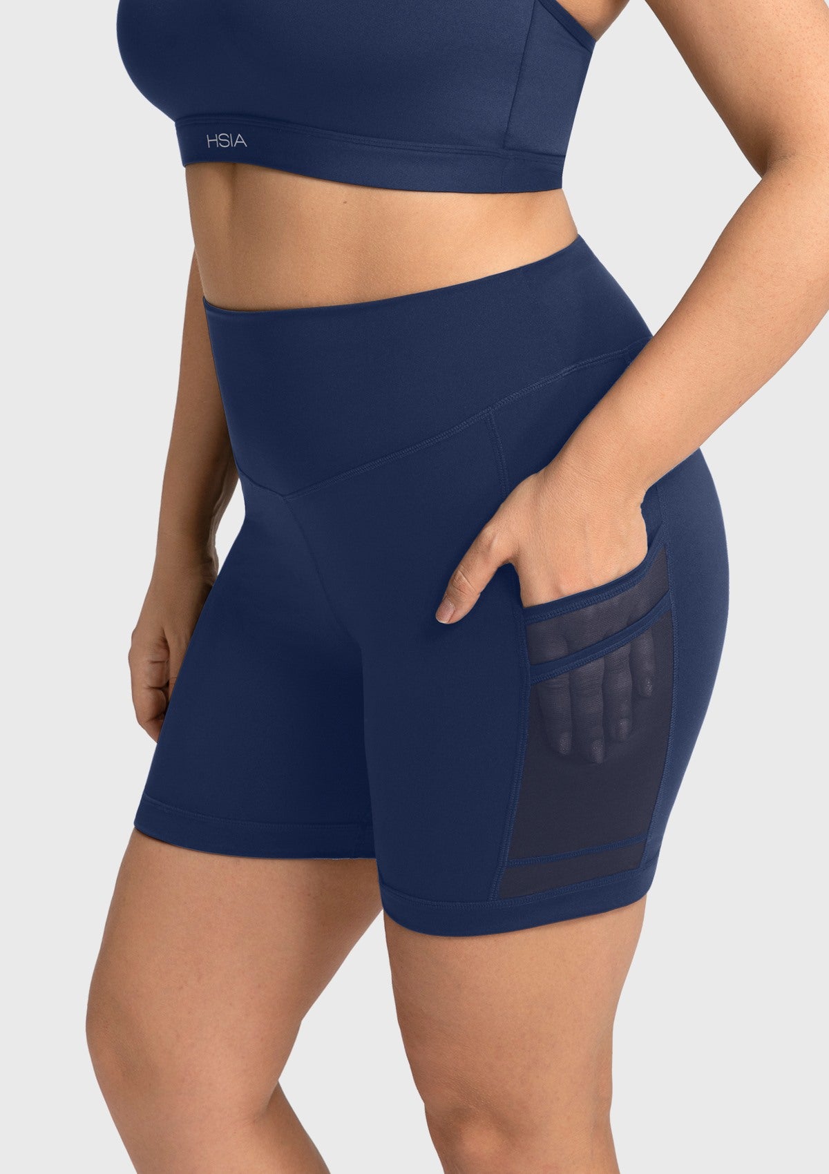 Side angle showing a woman using the handy pockets of the navy blue moisture-wicking activewear shorts, featuring innovative cooling fabric.