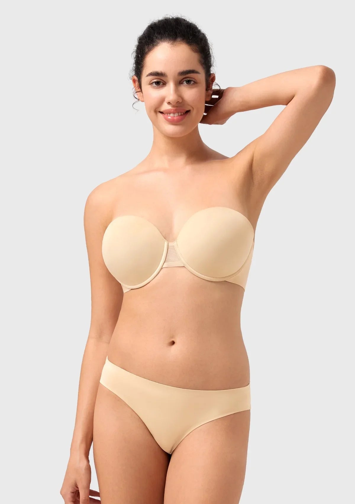 A confident woman raising her arms in the nude no-slip strapless bra, showcasing the secure, hypoallergenic silicone grip that stays put all day.