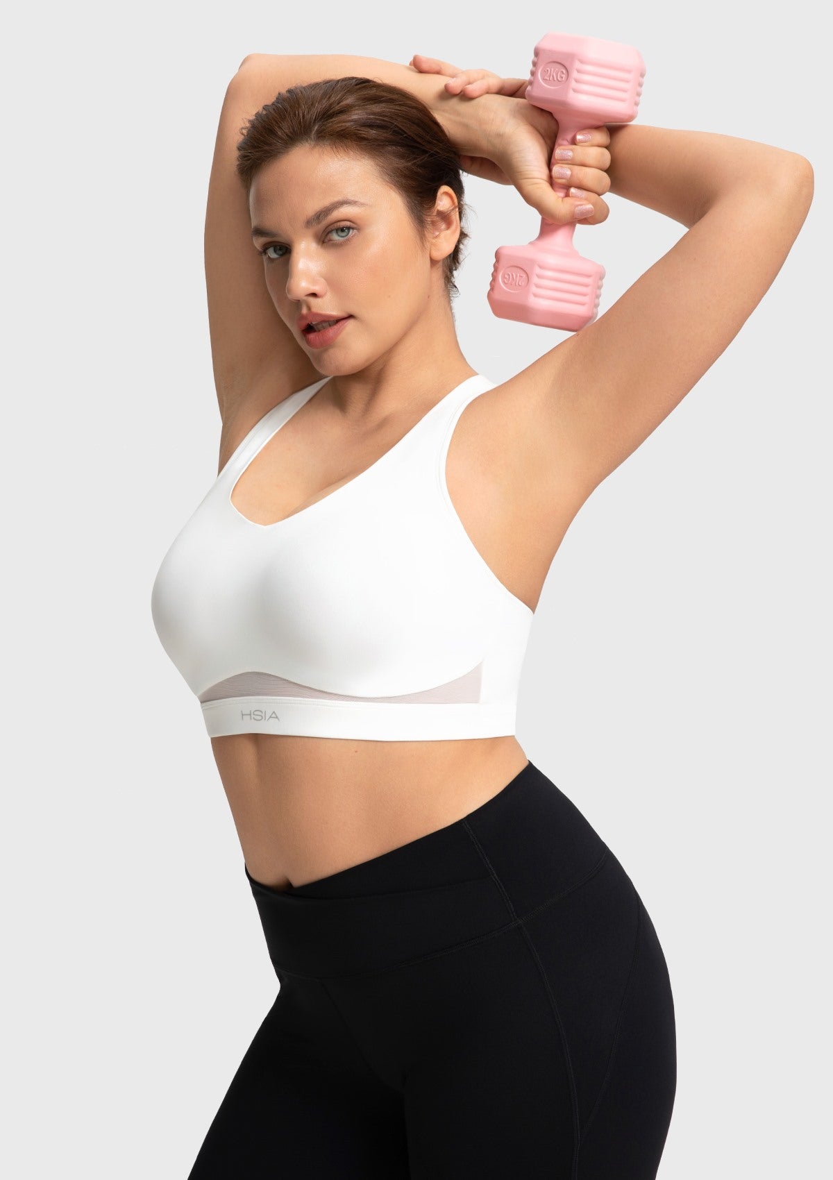 Woman lifting weights at the gym wearing the supportive and cooling white Aura sports bra