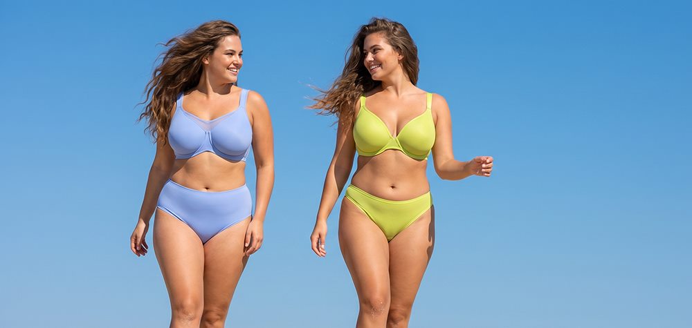 Two plus-size models walking outdoors under blue sky — one in periwinkle CoolComfort unlined minimizer bra, one in chartreuse Joan unlined t-shirt bra, both with matching bottoms