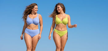 Two plus-size models walking outdoors under blue sky — one in periwinkle CoolComfort unlined minimizer bra, one in chartreuse Joan unlined t-shirt bra, both with matching bottoms