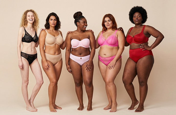 A diverse group of five smiling women standing in a row, confidently wearing comfortable, non-padded HSIA bras that provide a natural silhouette without showing nipples through their shirts.