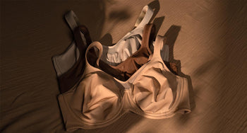 Three supportive bras in nude, brown and white flat lay on warm wood surface, showing everyday comfortable options for large busts