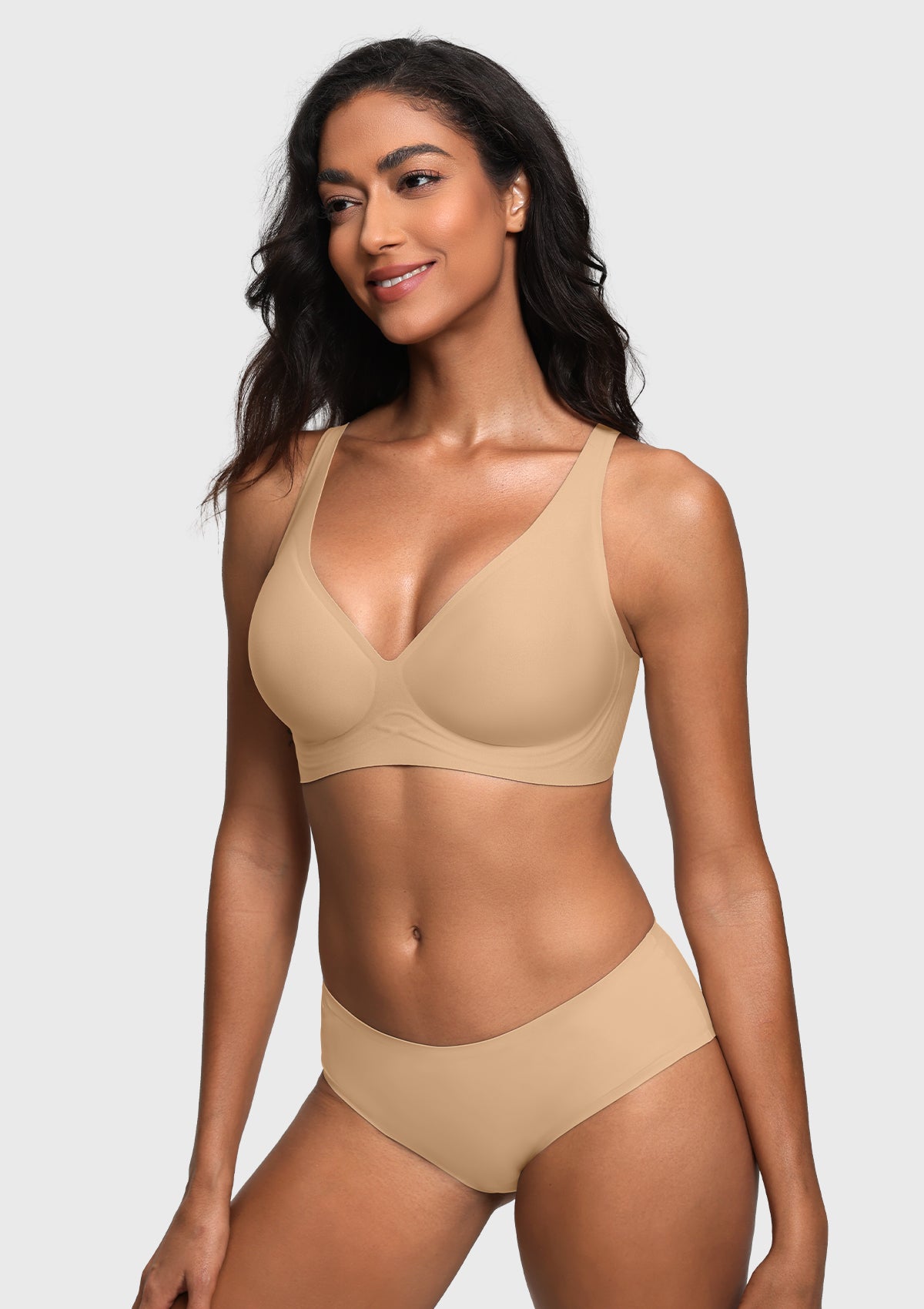 A woman modeling a matching light beige bra and high-waisted brief set against a light gray studio background.