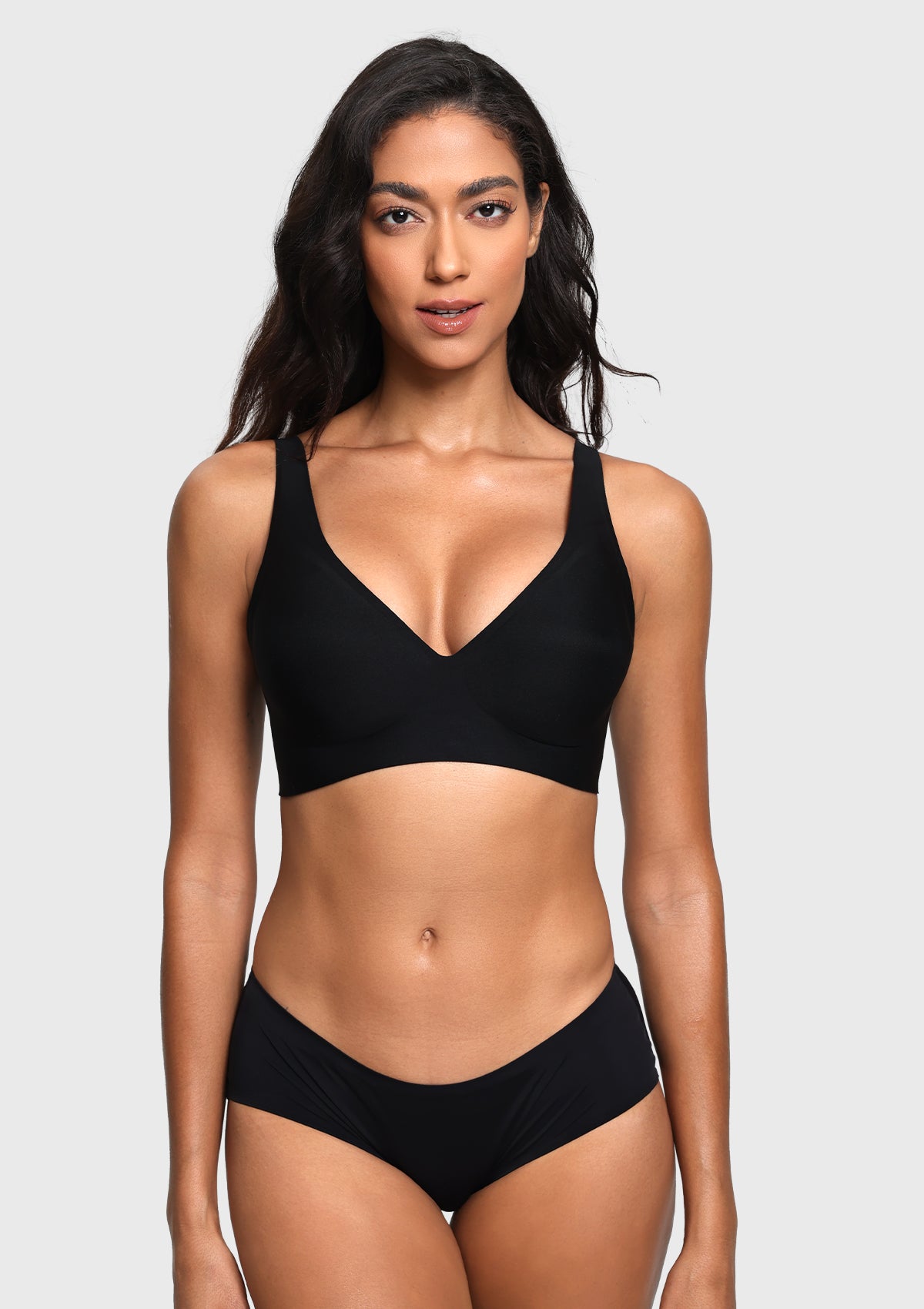 A woman modeling a black two-piece bikini set against a light gray studio background. The set includes a V-neck bikini top with wide shoulder straps and matching high-cut bikini bottoms.