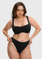 A woman modeling a solid black two-piece bikini set against a light gray studio background.