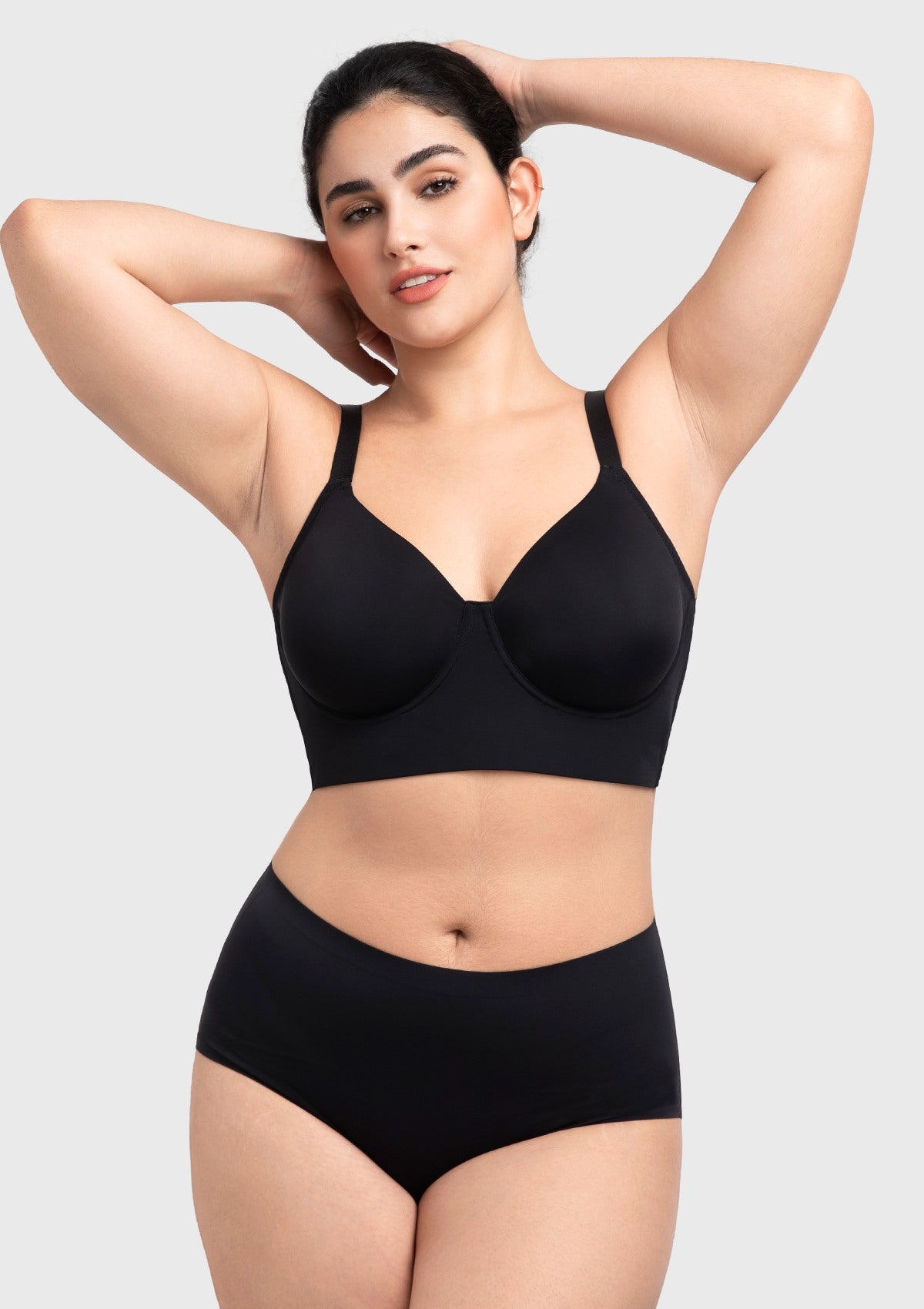 Smiling woman wearing the black minimizing bra, designed to naturally redistribute breast tissue without flattening