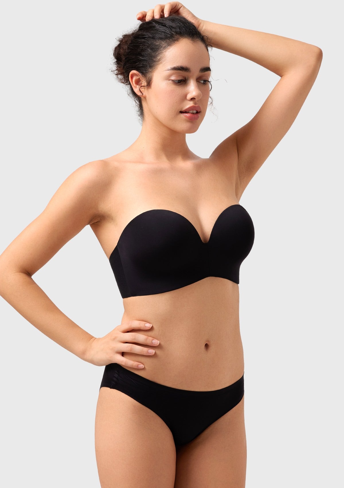 Three-quarter view of a woman raising her arms in the black seamless wireless bra, revealing the wide back-smoothing support wings.