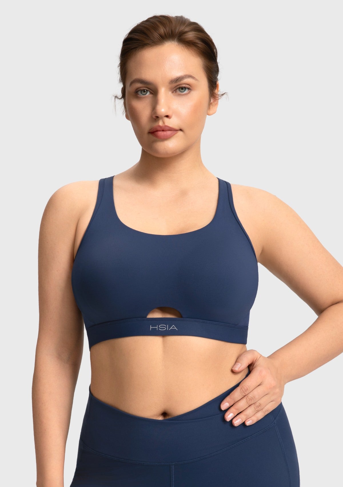 Front view of woman wearing the navy blue Aura criss-cross sports bra with breathable keyhole