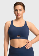 Front view of woman wearing the navy blue Aura criss-cross sports bra with breathable keyhole